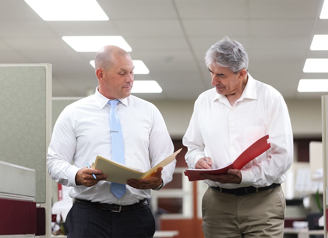 Our Process - Two Senior Employees at Rue Insurance Holding Folders and Disussing Strategy While Walking in the Office