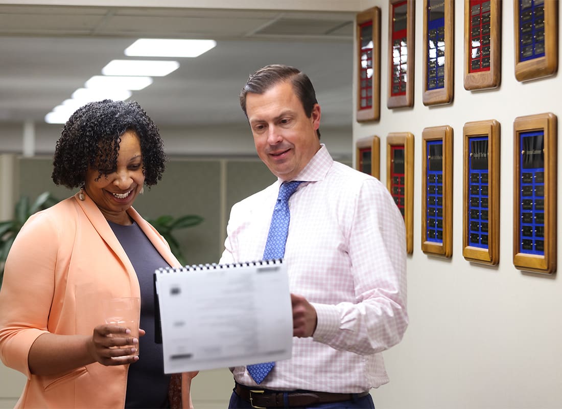 Read Our Reviews - Cheerful Male and Female Employees Looking at a Binder Inside the Rue Insurance Office